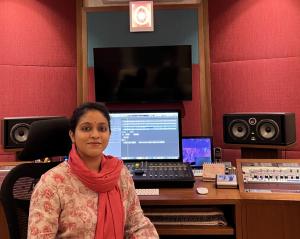 Young lady in sari sitting at recording studio console in colorful red studio space.